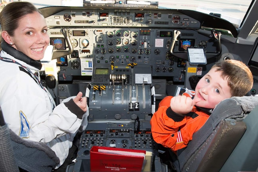 A staff member and the boy sitting in a plane cockpit.