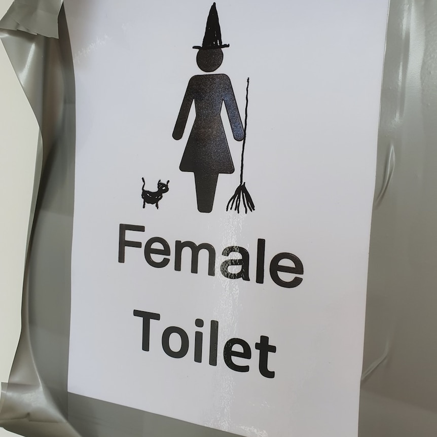 A sign for a women's bathroom with a witch's hat and broomstick added.