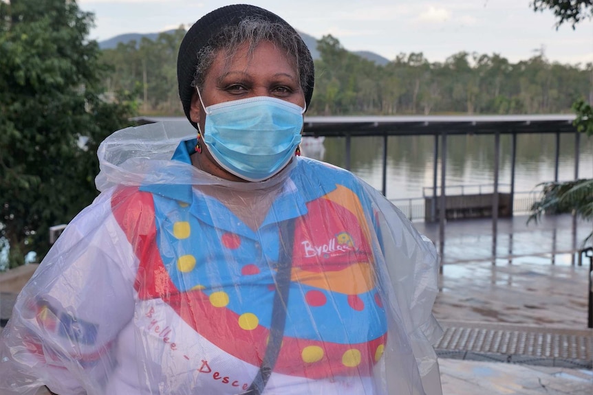 Annette Dudley stands on the Rockhampton riverbank wearing a mask and rain poncho.