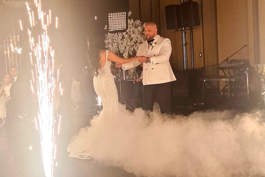 A bride and groom dancing with sparklers and smoke machine around them.