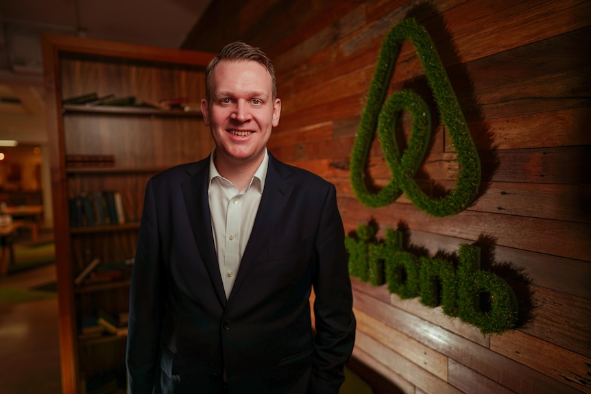 A man smiles in front of an airbnb sign