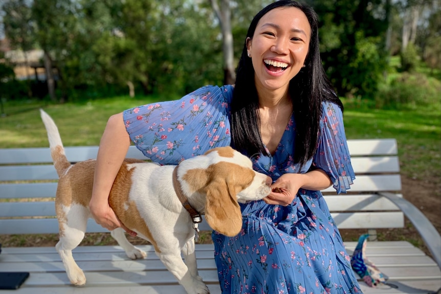 Tu Le sits on a bench smiling with her dog