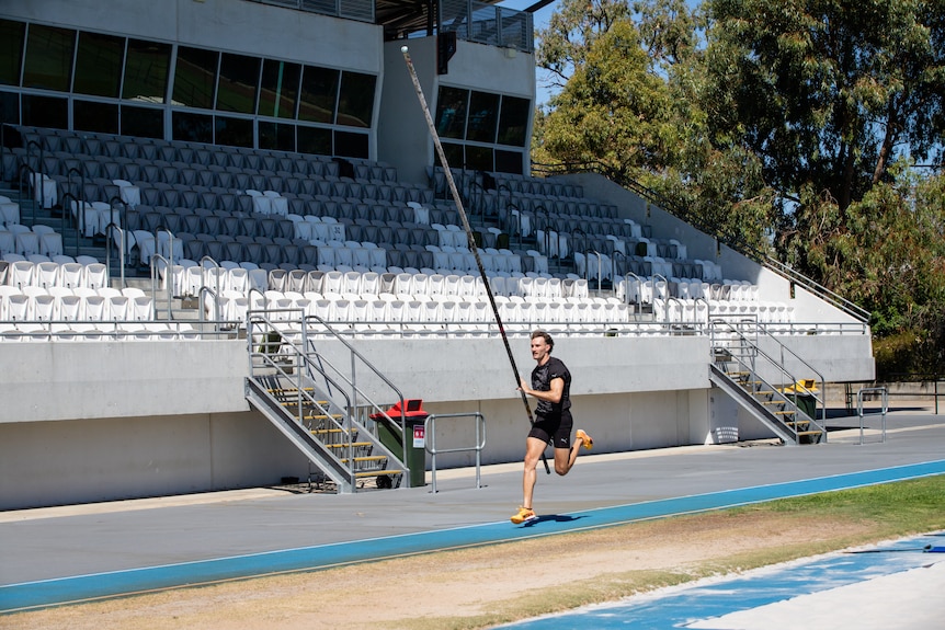 A man in activewear trains at an athletics stadium on a sunny day.