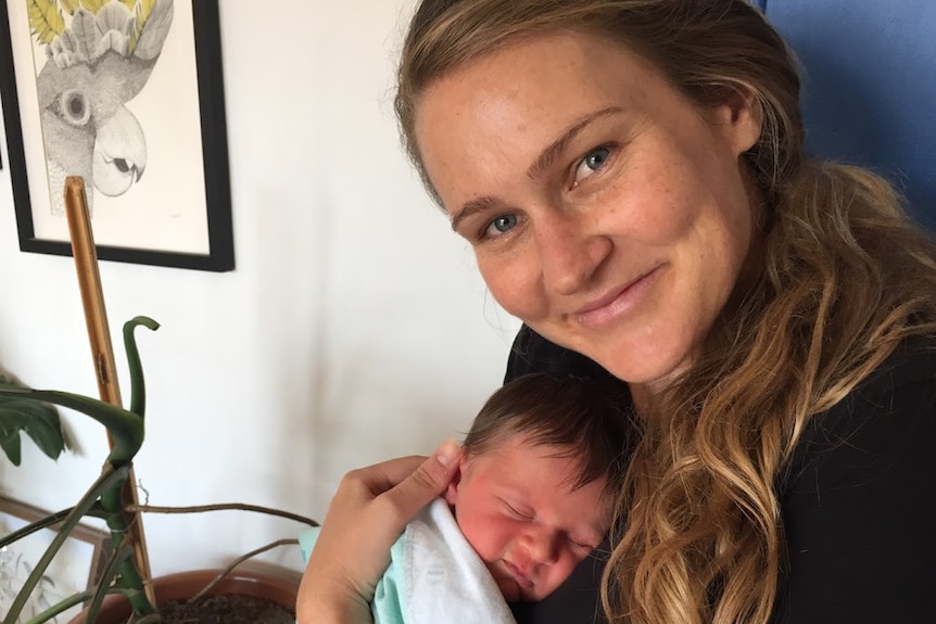 A smiling women holding a newborn baby.