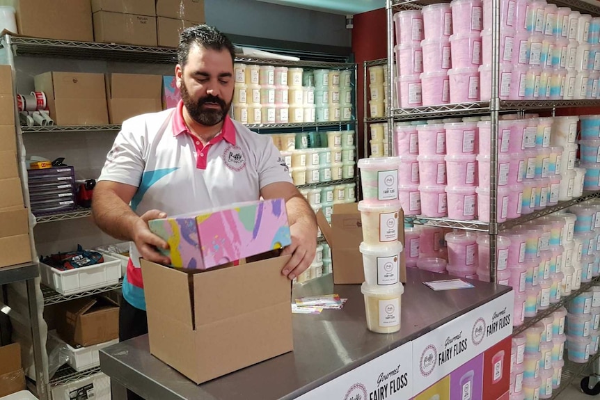 Michael packs a box in his shop surrounded by buckets of coloured fairy floss.