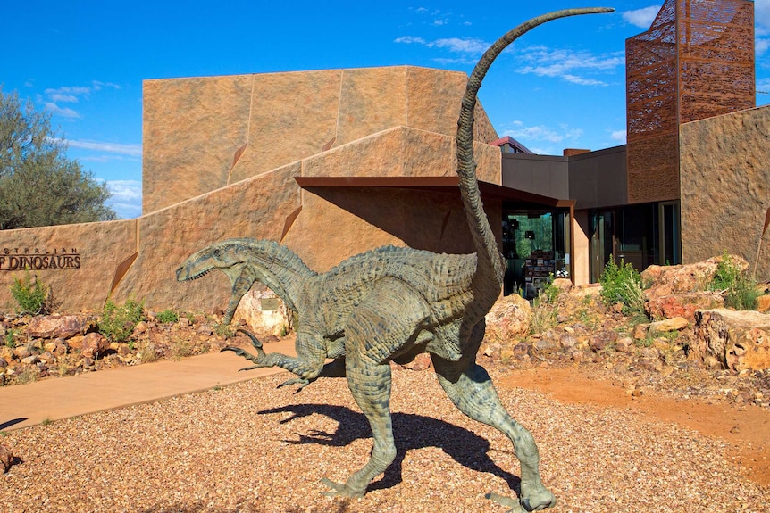 Daytime photograph of the entrance to the Age of Dinosaurs museum, which shows a life size statue of a raptor.