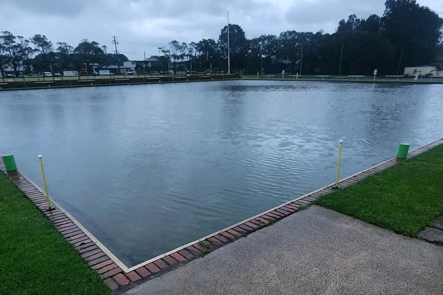 A flooded bowling green beneath a cloudy sky.