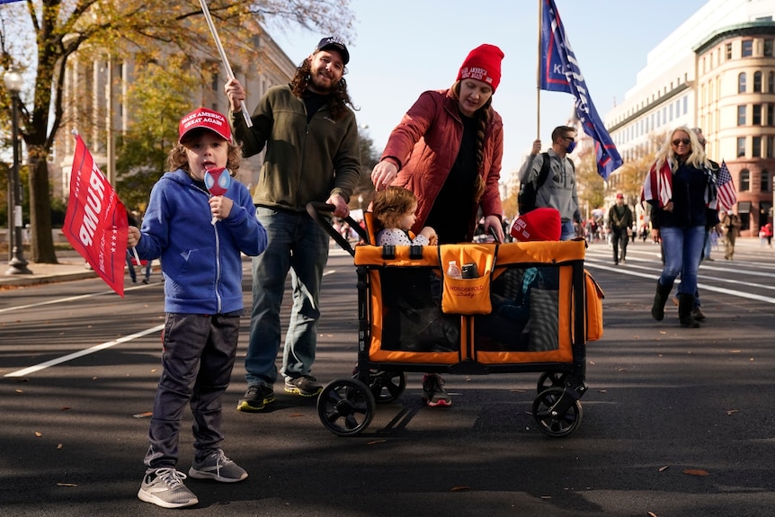 A family stands on a street with trump flags and children in a stroller