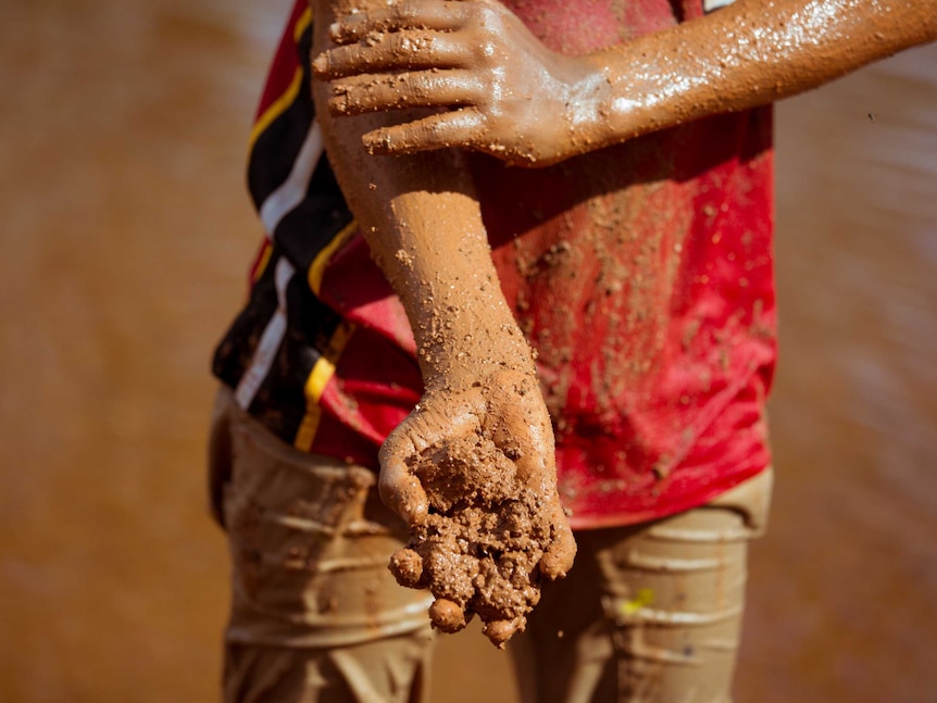 Junior rubs mud into his skin.
