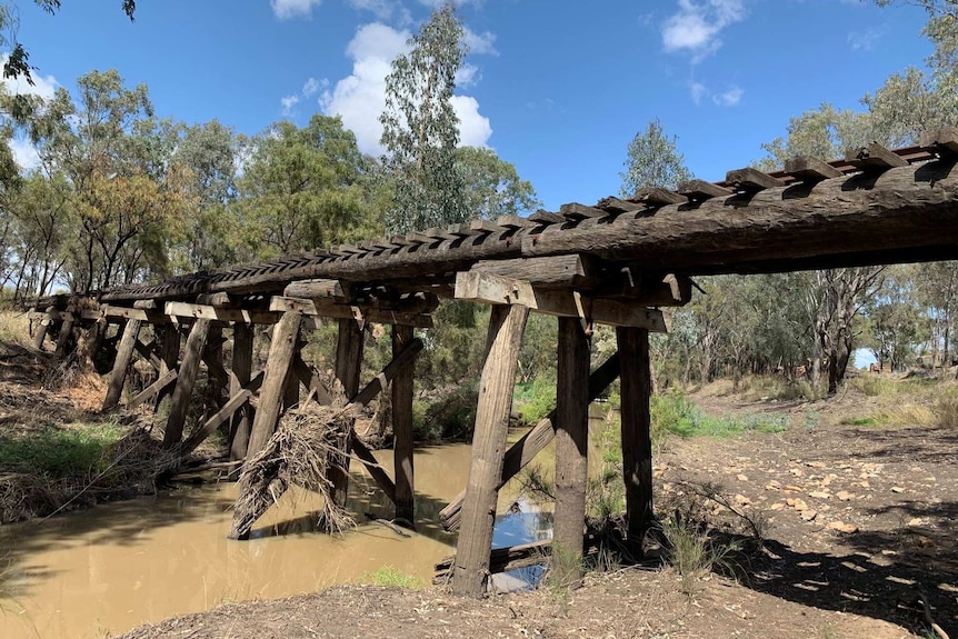 An old wooden rail bridge running across a creek that holds a little bit of water
