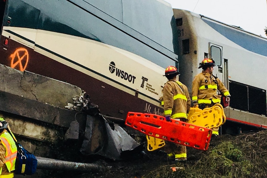 Emergency workers carry stretchers next to a derailed train.