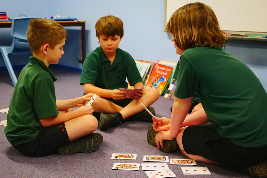 Three boys sitting in circle playing game of cards.