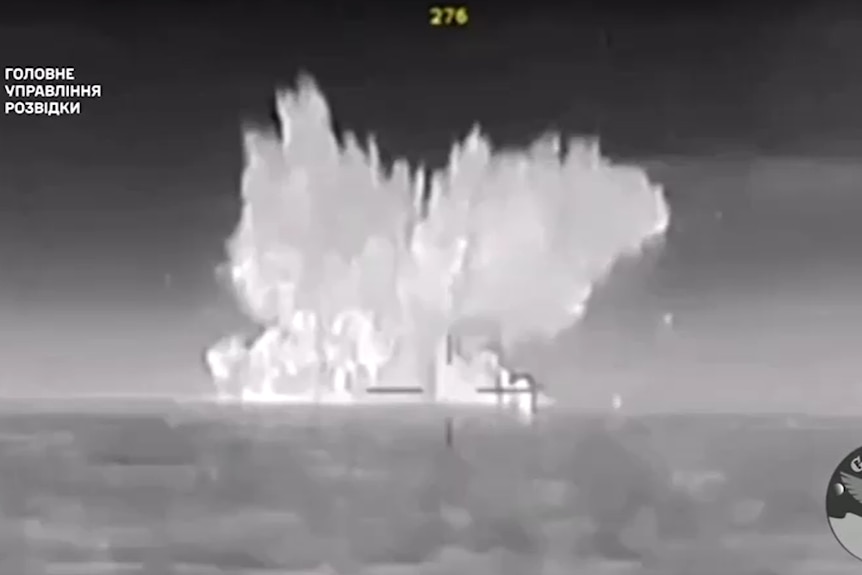 Black and white footage at sea that appears to show an explosion in the distance.