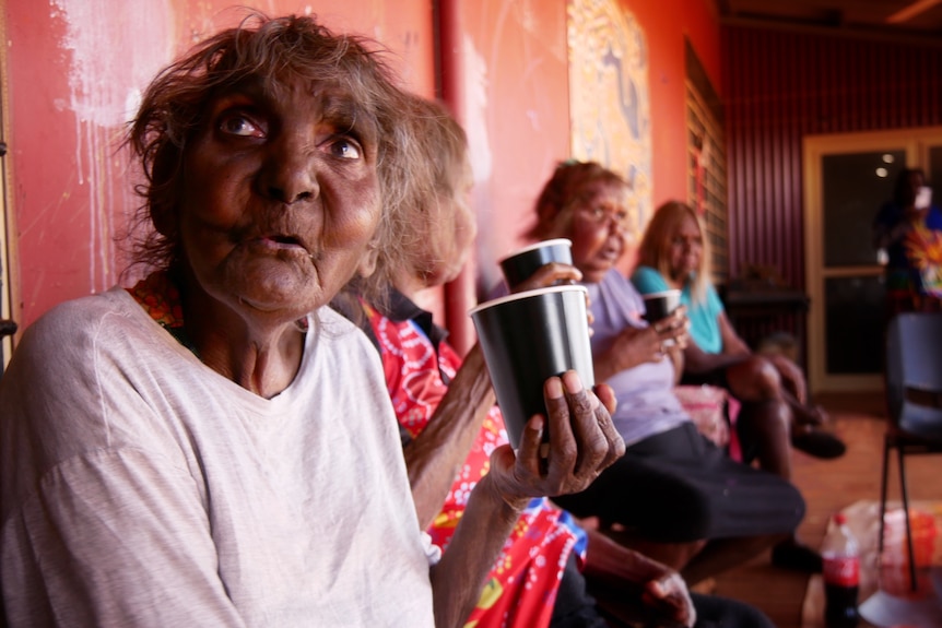 A group of elders drinking from cups on a bench in Balgo, August 2022. 