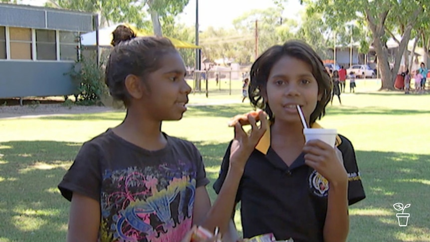 2 Aboriginal girls - one eating fruit and the other drinking from a cup with a straw