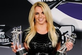 Britney spears postes holding two awards statues shaped like astronauts 