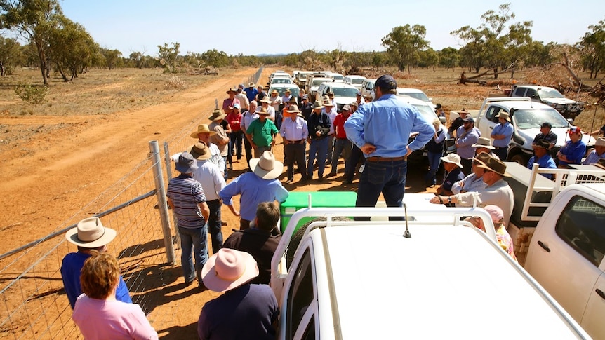 Farmers standing next to a fence on the red soil of western NSW listening to speakers talk about its construction.