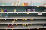 A row of shelves in a US supermarket, with only a few cans of baby formula on display 