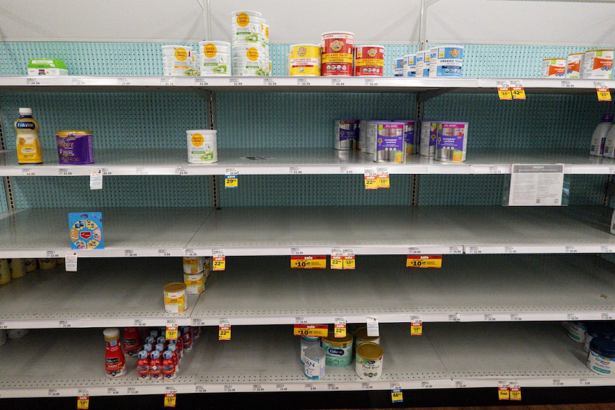 A row of shelves in a US supermarket, with only a few cans of baby formula on display 
