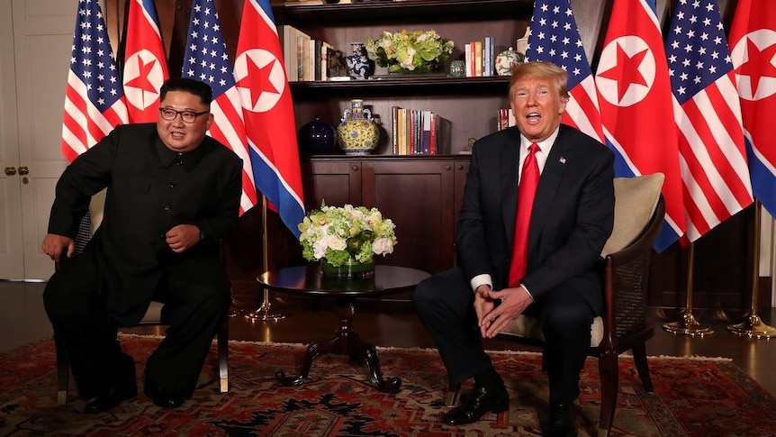 Kim Jong-un and Donald Trump seated together with their country's flags behind them.