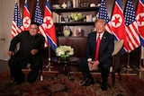 Kim Jong-un and Donald Trump seated together with their country's flags behind them.