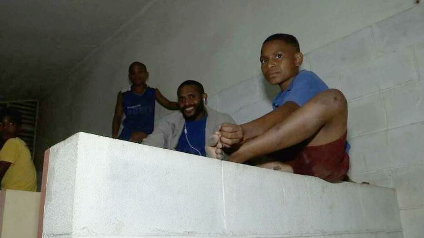 A number of young and older boys are seen sitting in a public toilet cubicle.