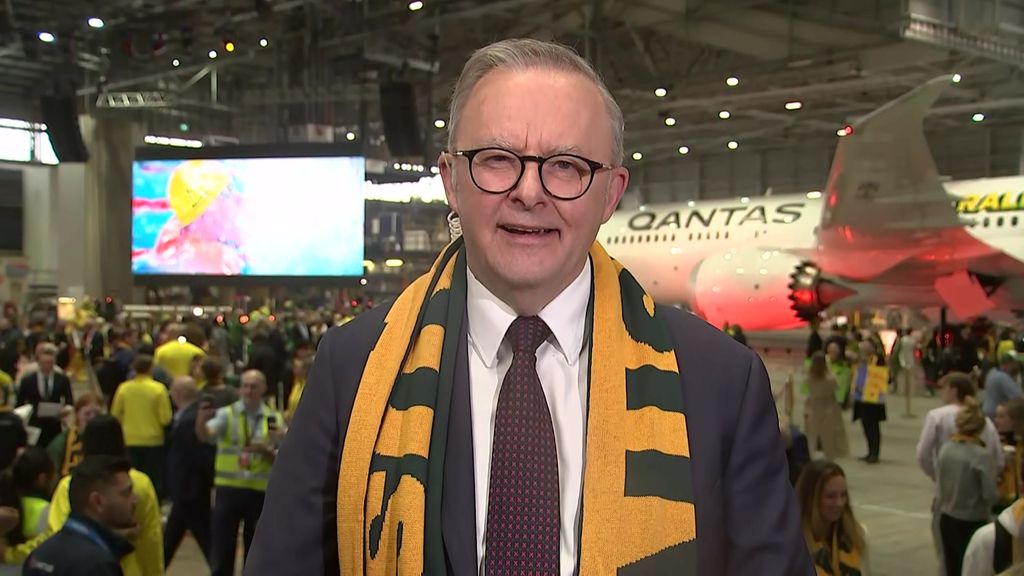 Prime Minister smiling, wears green and gold scarf on tarmac 