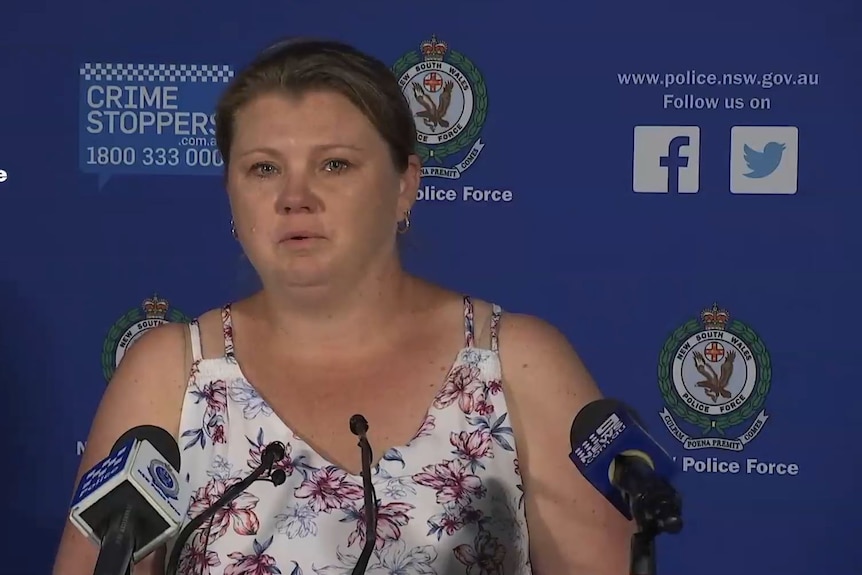 A heavyset woman with brown hair tied back, white blouse, stands before several microphones at a police press conference