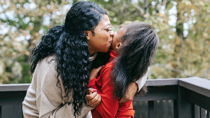 A woman hugs and kisses a young girl for a story on early puberty in children.