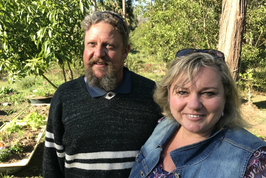 Marcus and Sharon Koski smile at the camera with a fruit tree, a garden bed and bush in the background.