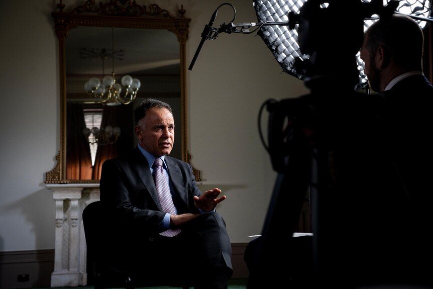 John Pesutto sits in a chair, speaking to a journalist who is in shadow.