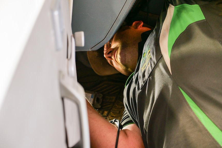 A mechanic wearing a cap works on a car.
