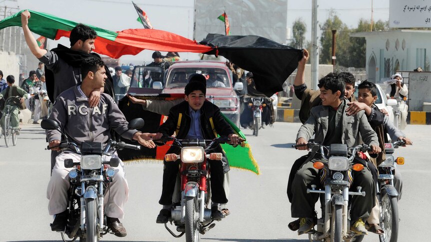 Afghan cricket fans ride down the street on motorbikes while flying flags