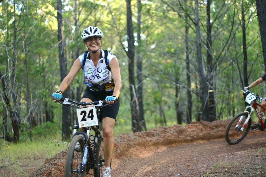 a woman on a mountain bike riding in a competition in a pine forest.