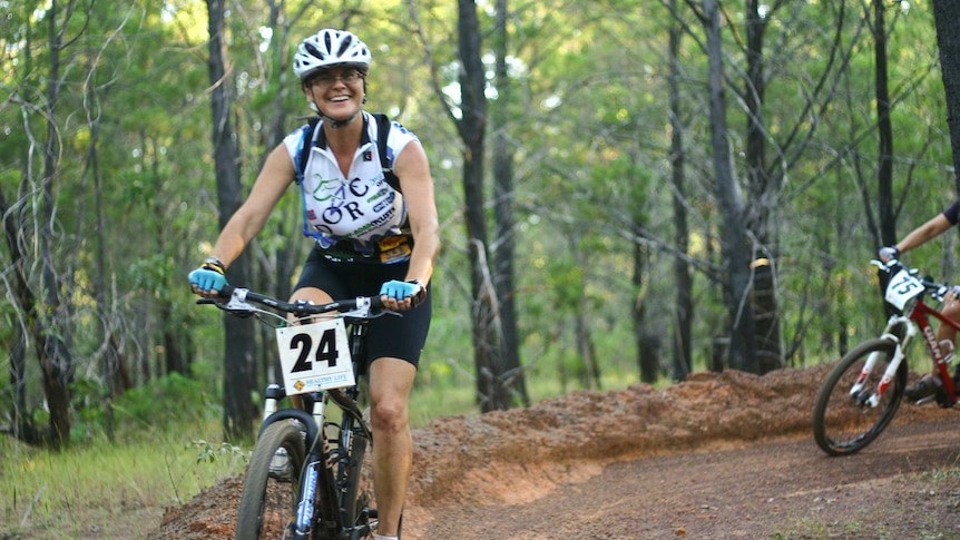 a woman on a mountain bike riding in a competition in a pine forest.