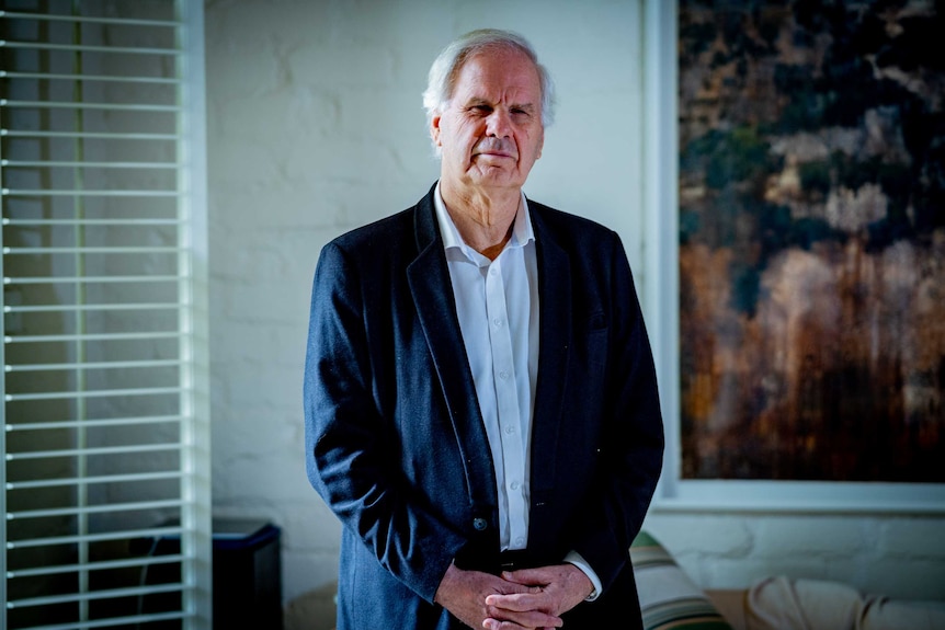 An older man in a suit looking at a camera in his home environment.