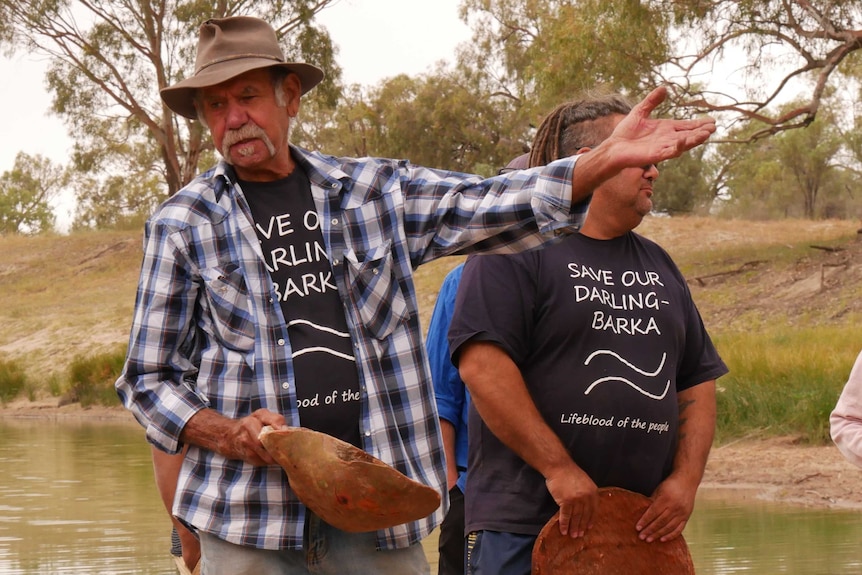 Barkindji elder Badger Bates talking to an unseen group of people, with a coolemon in his right hand
