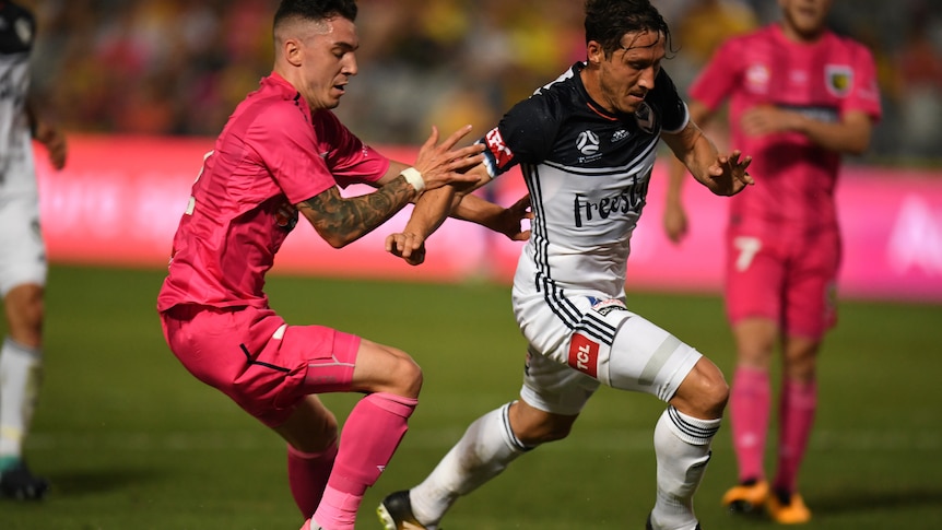 Central Coast Mariners' Storm Roux pressures Melbourne Victory's Mark Milligan