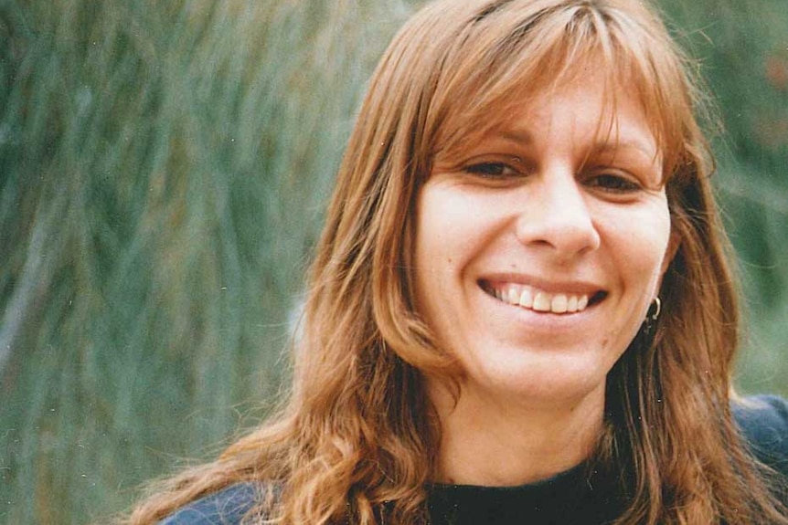 Indigenous poet Ali Cobby Eckermann smiles as she poses for a photo in front of trees.