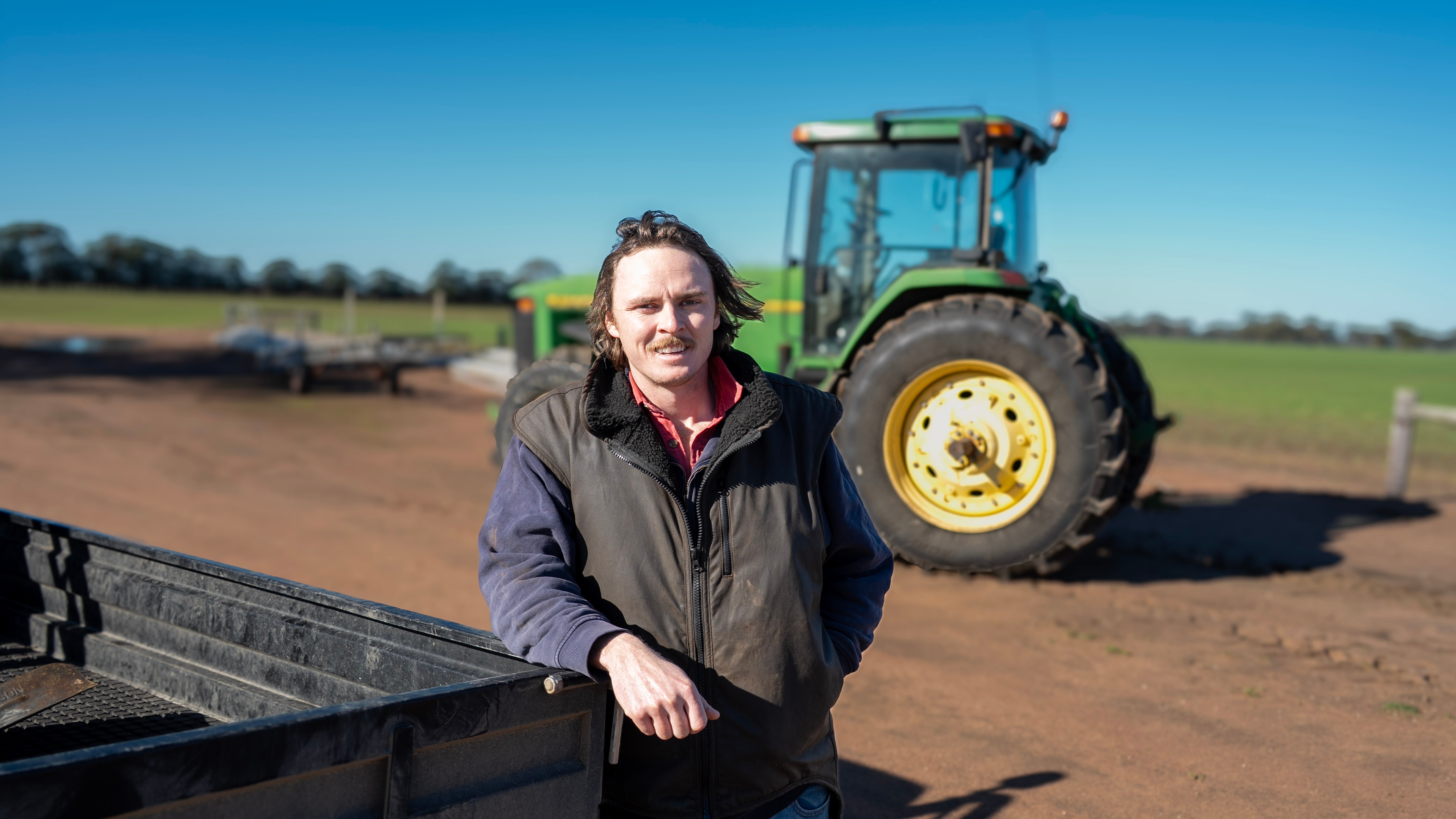 A man leaning against a ute and standing in front of a tractor.