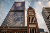 Historic brick clocktower rises with cloudy sky and modern skyscraper behind
