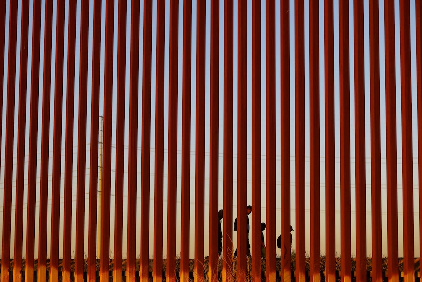 A big rust coloured gate is pictured, behind it the silhouettes of two adults and two children.