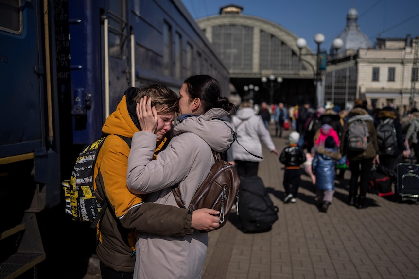 A woman embraces a teenage boy getting off a train. 
