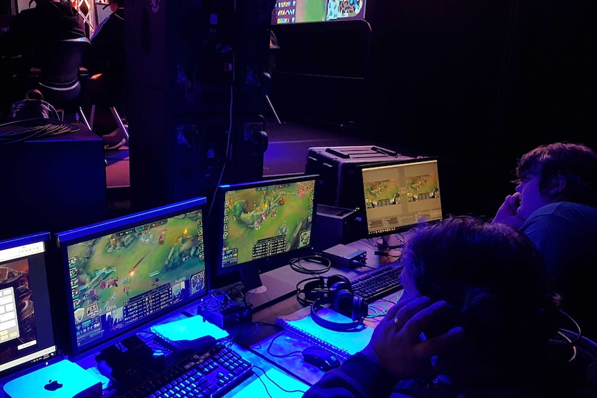 Two students sitting in front of computer screens playing a video game.