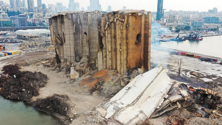 A large section of concrete lays on the ground next to a damaged concrete structre that sits before a city skyline