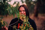 Rachael McPhail, who campaigned for Australia Post to include First Nations place names, smiling behind a wattle tree at sunset.