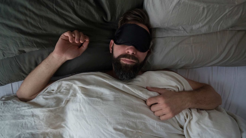 High angle view of man wearing sleep mask while sleeping on bed at home.
