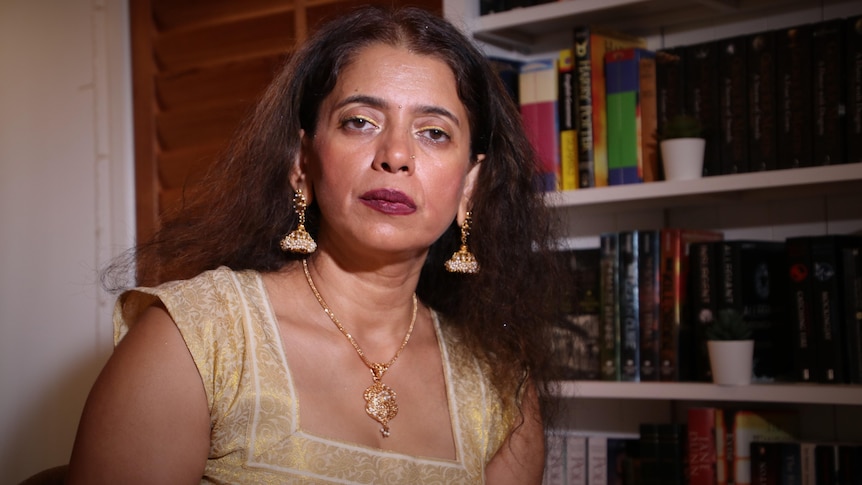 a woman in a gold top iht a bookcase behind her