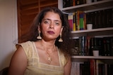 a woman in a gold top iht a bookcase behind her