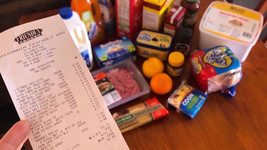 A receipt from a supermarket totalling $131.70 with a table full of groceries in the background.